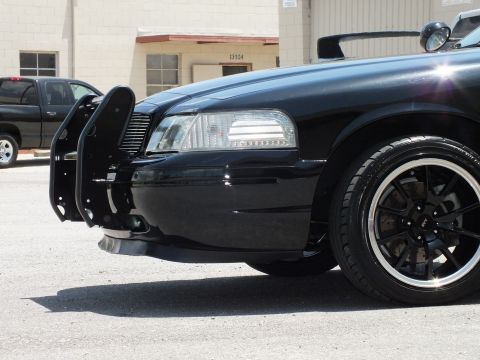 2003 Ford Crown Victoria - Low front-quarter detail of a black sedan with brush guard and dark polished wheel.