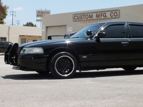 2003 Ford Crown Victoria - Low-angle front-quarter of a black sedan on machined-lip wheels beside an industrial building.