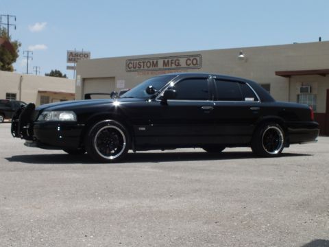 2003 Ford Crown Victoria - Side profile of a lowered black sedan with push bumper on dark polished-lip wheels.