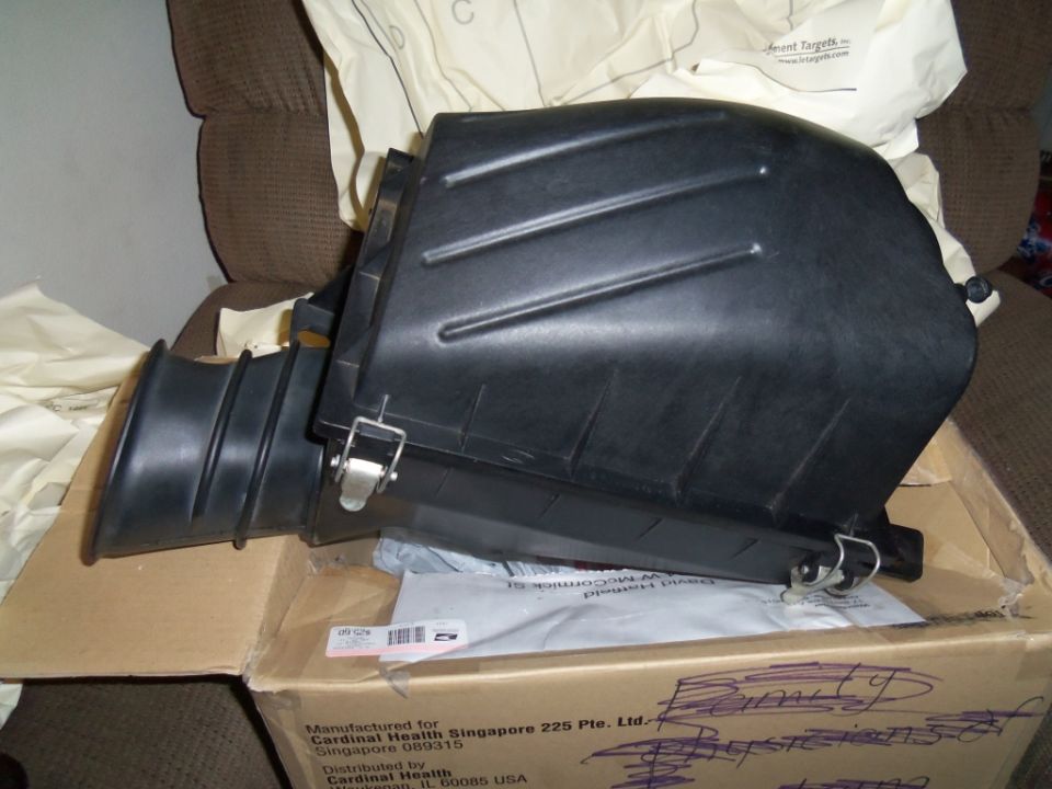 black plastic air intake housing with ribbed hose attached, sitting in a cardboard box