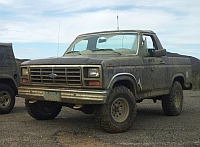 1986 Ford Bronco - A dusty 1980s Ford Bronco is parked next to another vehicle under a cloudy sky.