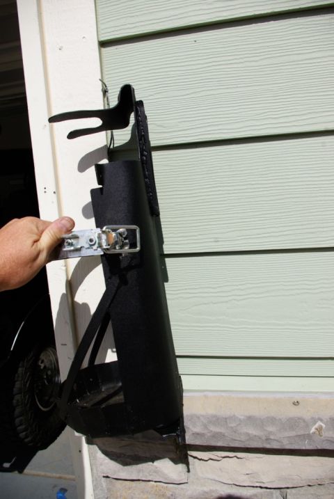 1995 Ford Bronco - A black metal part, possibly a step or bracket, is held by a hand against a house exterior.