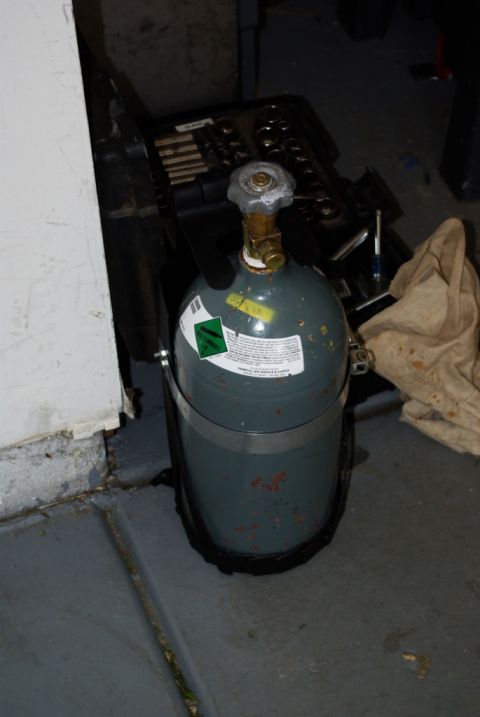 1995 Ford Bronco - A gas cylinder sits on a concrete floor next to a toolbox and a cloth bag.