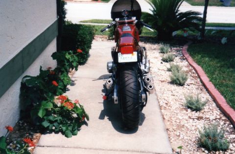1999 Ford Ranger - Rear view of a red motorcycle parked on a sidewalk with landscaping.