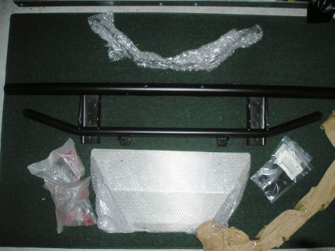 1999 Ford Ranger - A collection of vehicle parts, including a black metal bumper and various fasteners, are arranged on a carpeted floor.