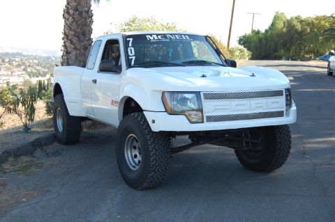 1999 Ford Ranger - A modified white pickup truck with off-road tires is parked on a hill overlooking a town.