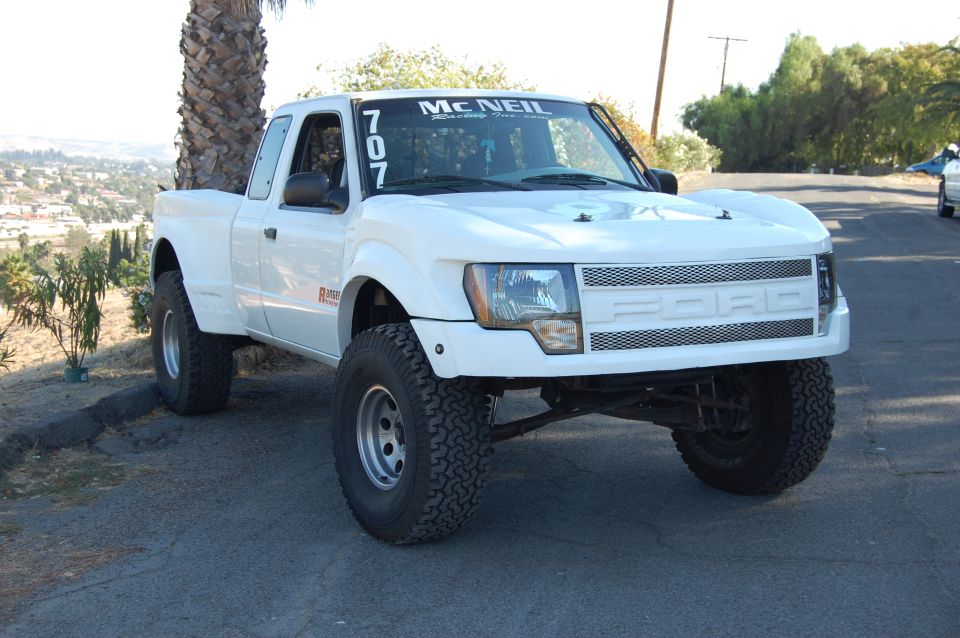 White pickup truck with McNeil sticker on windshield and '707' numbers. It has a custom grille with 'FORD' lettering