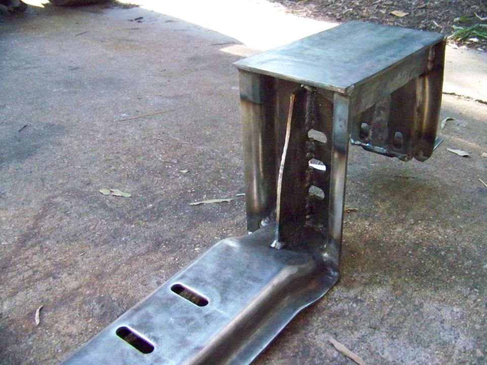 Metal bracket with welded seams and slotted holes, resting on concrete