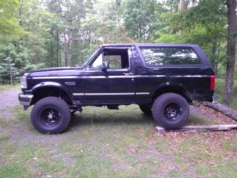 1995 Ford Bronco - This black 1995 Ford Bronco is shown from the side, parked outdoors in a wooded area.