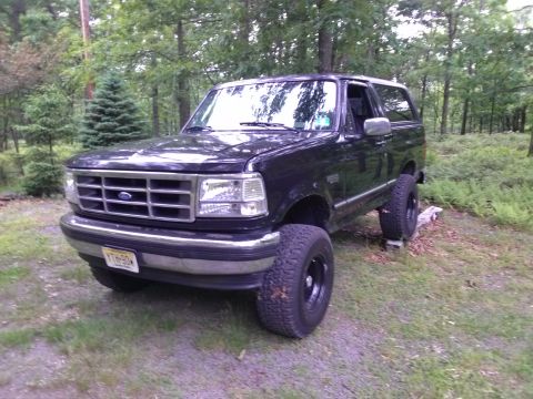 1995 Ford Bronco - 1995 Ford Bronco XLT with aftermarket wheels sits in a forest clearing.