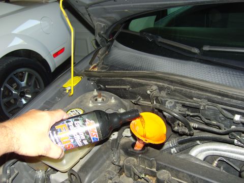 2007 Ford Mustang - A person pours fluid into the engine bay of a car, with another car visible in the background.