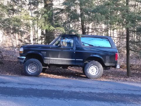 1995 Ford Bronco - A black 1995 Ford Bronco is parked on the side of a wooded road.