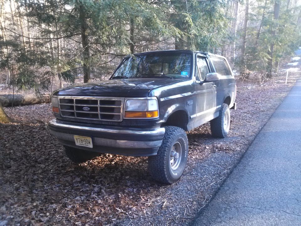 Black 1995 Ford Bronco parked on a dirt road next to trees