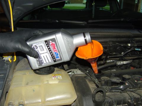 2007 Ford Mustang - Pouring AMSOIL synthetic motor oil into the engine via a funnel. The vehicle year is not identifiable from the image.