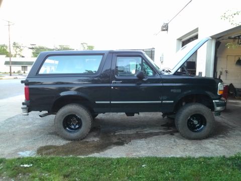 1995 Ford Bronco - This black Ford Bronco is parked on a concrete pad with grass nearby.