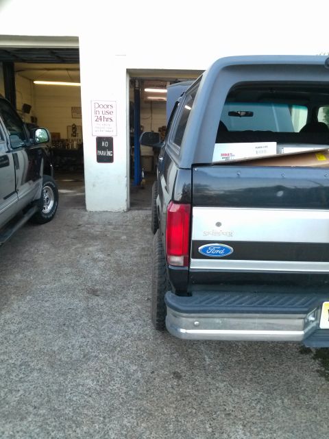 1995 Ford Bronco - Rear view of a black Ford Bronco with a silver stripe and aftermarket cap, parked next to another vehicle in a garage.
