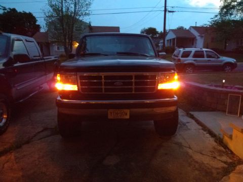 1995 Ford Bronco - A dark Ford Bronco is parked in a driveway at dusk, with its front turn signals illuminated.