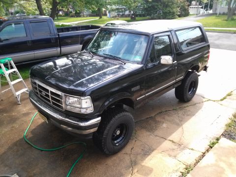 1995 Ford Bronco - A black Ford Bronco is parked on a cracked concrete driveway with a green hose on the ground.