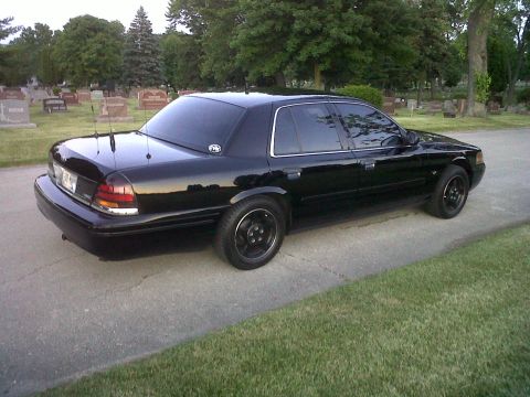 1999 Ford Crown Victoria - A black 1999 Ford Crown Victoria is parked on a road with gravestones in the background.
