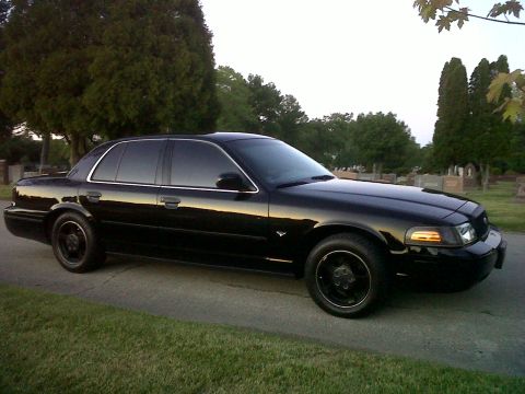 1999 Ford Crown Victoria - A black sedan sits in a cemetery, its reflection visible on the polished surface.