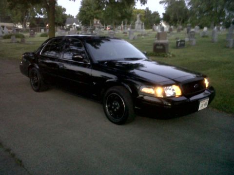1999 Ford Crown Victoria - Black Ford Crown Victoria parked on asphalt in a cemetery with tombstones visible.
