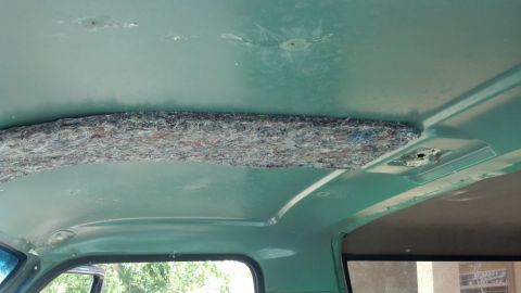 1995 Ford Bronco - The interior ceiling of a vehicle shows exposed insulation and a Supermotors logo on the window.