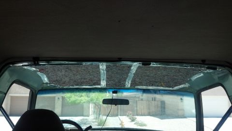 1995 Ford Bronco - View from inside a vehicle, looking through a damaged windshield at houses and trees.