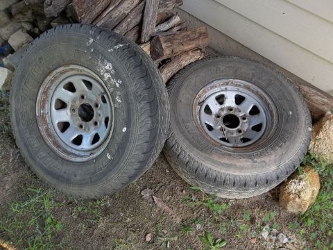 1995 Ford Bronco - Two tires and rims are shown outdoors, leaning against a wall and stacked wood.