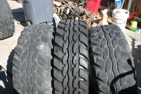 1991 Ford Bronco - Three off-road tires are displayed outdoors, with various vehicle parts and a trash can visible.