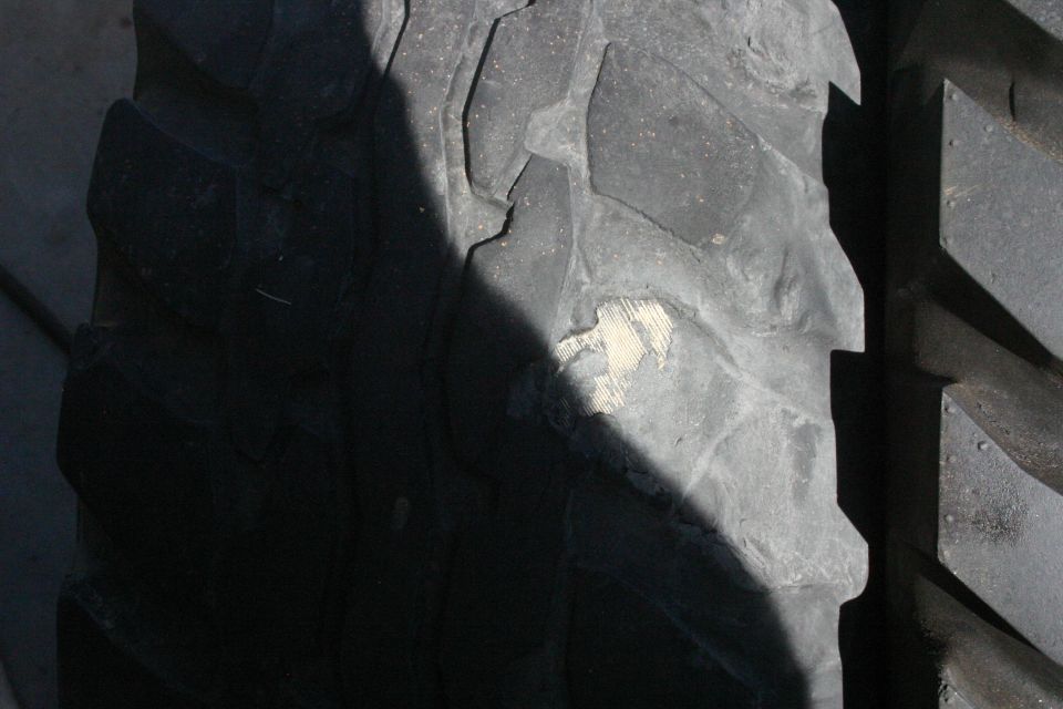 Close-up of a large tire tread with a shadow across it and a scuff mark