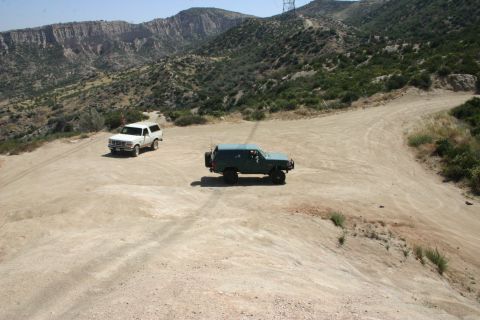 1991 Ford Bronco - Two Ford Broncos are parked on a dirt road in a mountainous, arid landscape.