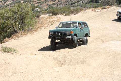 1991 Ford Bronco - This lifted 1991 Ford Bronco navigates a sandy off-road course, with another vehicle visible in the background.