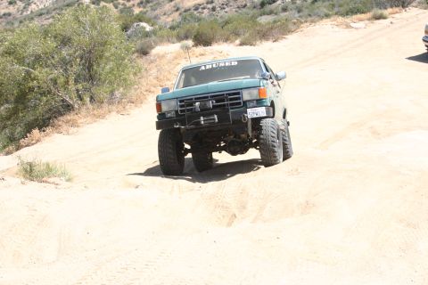 1991 Ford Bronco - Modified truck with lifted suspension navigates a sandy trail. License plate visible.