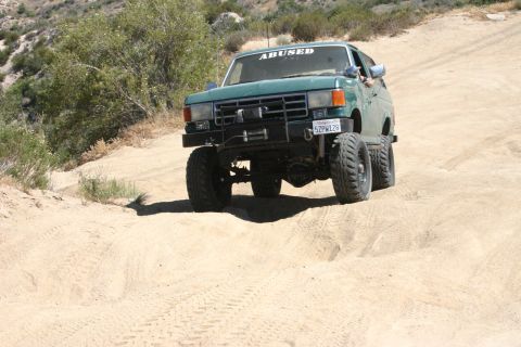 1991 Ford Bronco - This modified SUV navigates a sandy, off-road trail under a clear sky.