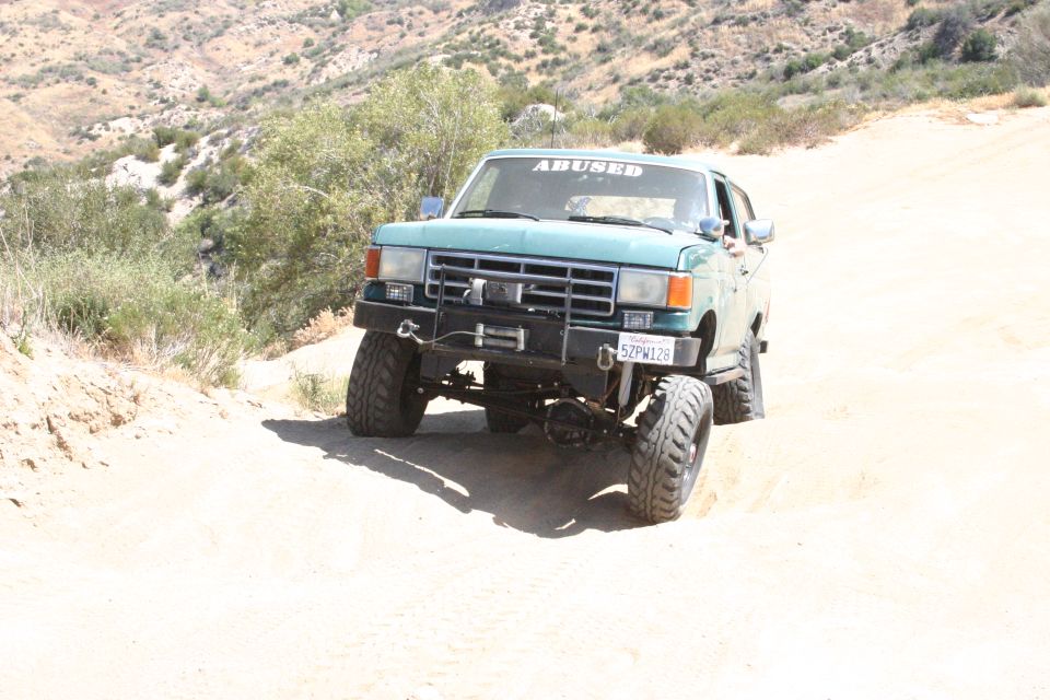 Teal Ford Bronco with "ABUSED" sticker on windshield, lifted suspension, and winch