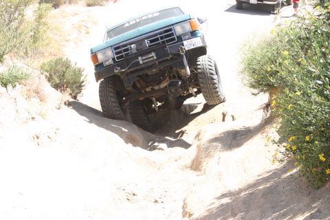 1991 Ford Bronco - A teal off-road truck navigates a challenging dirt path with a winch mounted on the front.