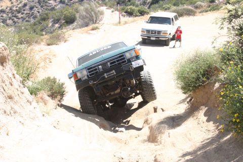 1991 Ford Bronco - A modified green 1991 Ford Bronco navigates a challenging off-road course, with another SUV visible in the background.
