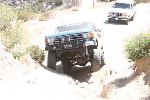 1991 Ford Bronco - Two Ford Broncos navigate a challenging off-road trail under a clear sky.