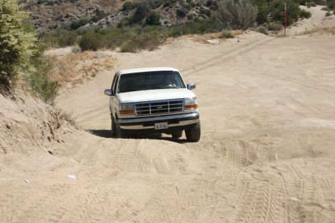 1991 Ford Bronco - White Ford F-Series truck navigates a dusty, off-road trail.