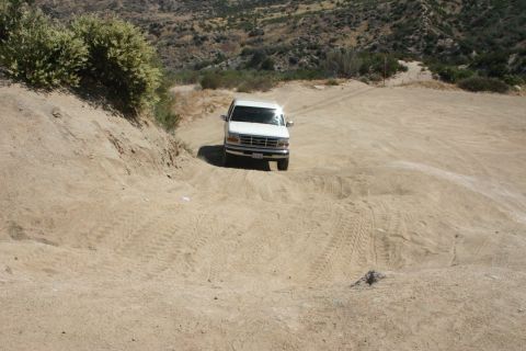 1991 Ford Bronco - White Ford Bronco navigates a steep, sandy incline with visible tire tracks.