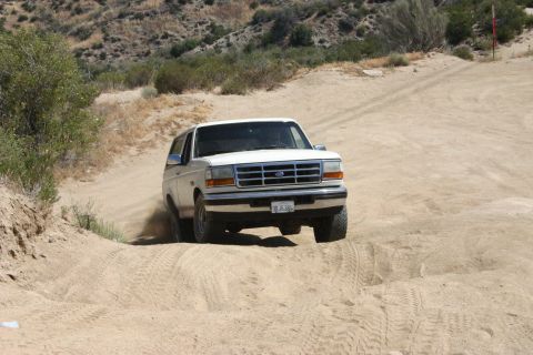 1991 Ford Bronco - This 1992 Ford Bronco is navigating a dusty, off-road trail with hills in the background.