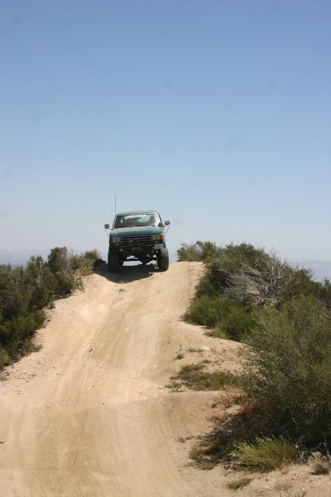 1991 Ford Bronco - A green SUV navigates a dusty trail under a clear blue sky.