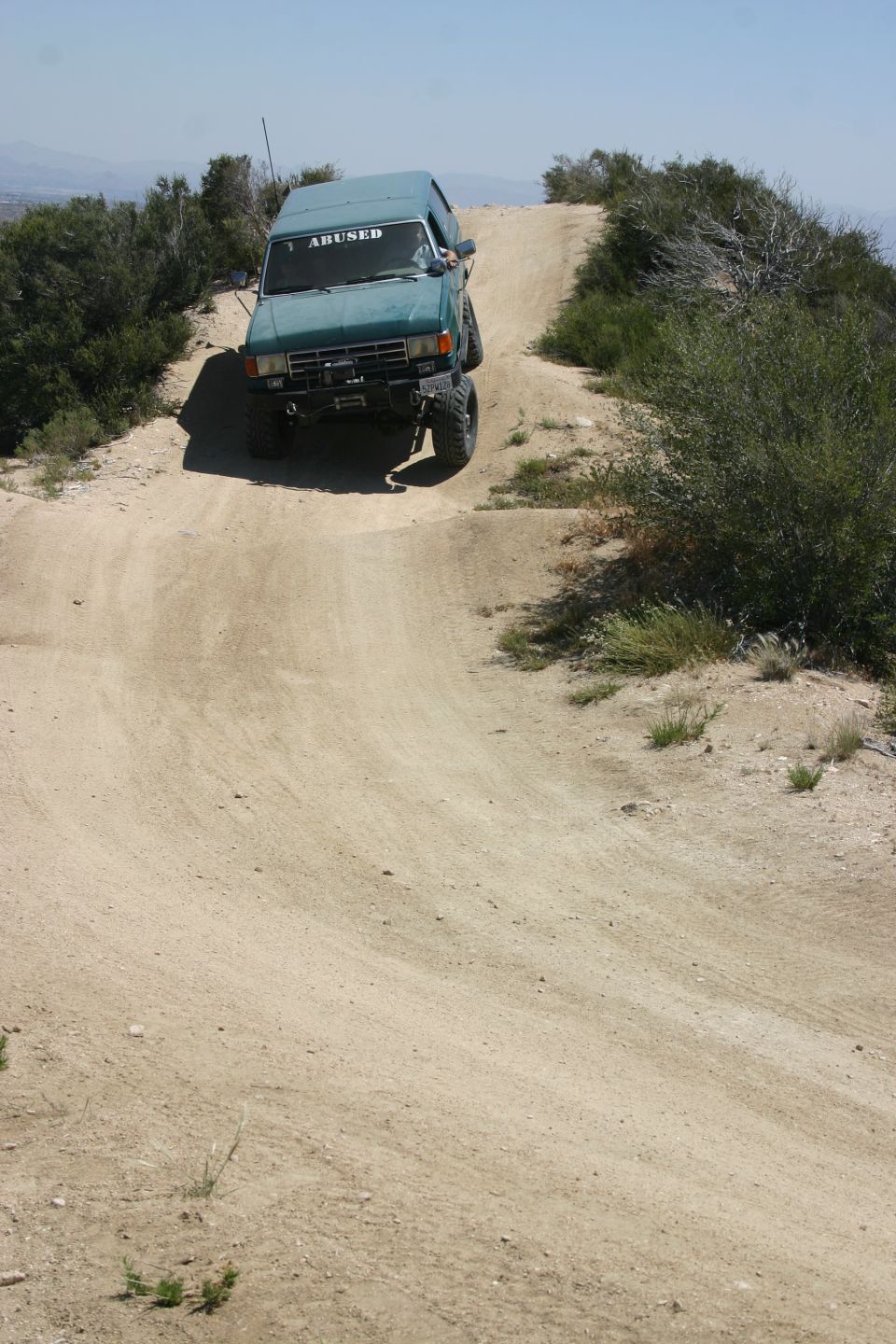 1991 Ford Bronco driving up a steep dirt hill, 'ABUSED' sticker on windshield