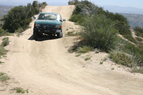 1991 Ford Bronco - A green SUV navigates a steep dirt path on a sunny day, with a winch mounted on the front bumper.