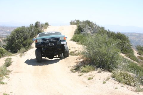 1991 Ford Bronco - This teal Ford F-Series truck navigates a dusty, off-road trail under a clear sky.