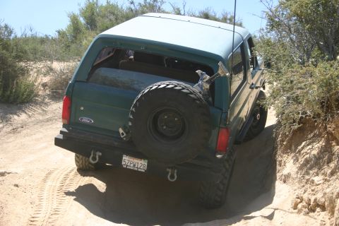 1991 Ford Bronco - This 1991 Ford Bronco is navigating a dusty, off-road trail with dry brush on the sides.