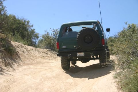 1991 Ford Bronco - A green Ford Bronco navigates a dusty trail under a clear blue sky.
