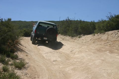 1991 Ford Bronco - A green 1991 Ford Bronco navigates a dusty trail with a spare tire mounted on the rear.