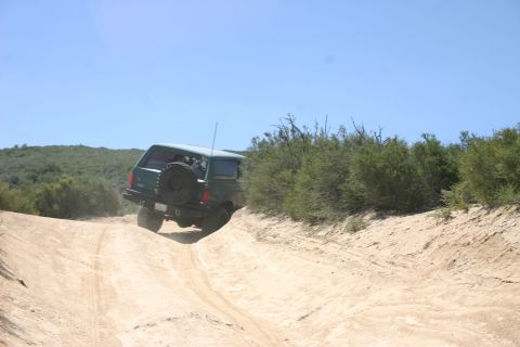 1991 Ford Bronco - 1991 Ford Bronco navigating a steep dirt trail with scrub brush and hills in the background.