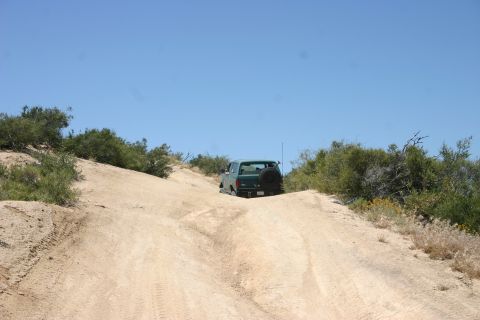 1991 Ford Bronco - A green SUV navigates a steep, sandy trail under a clear blue sky.